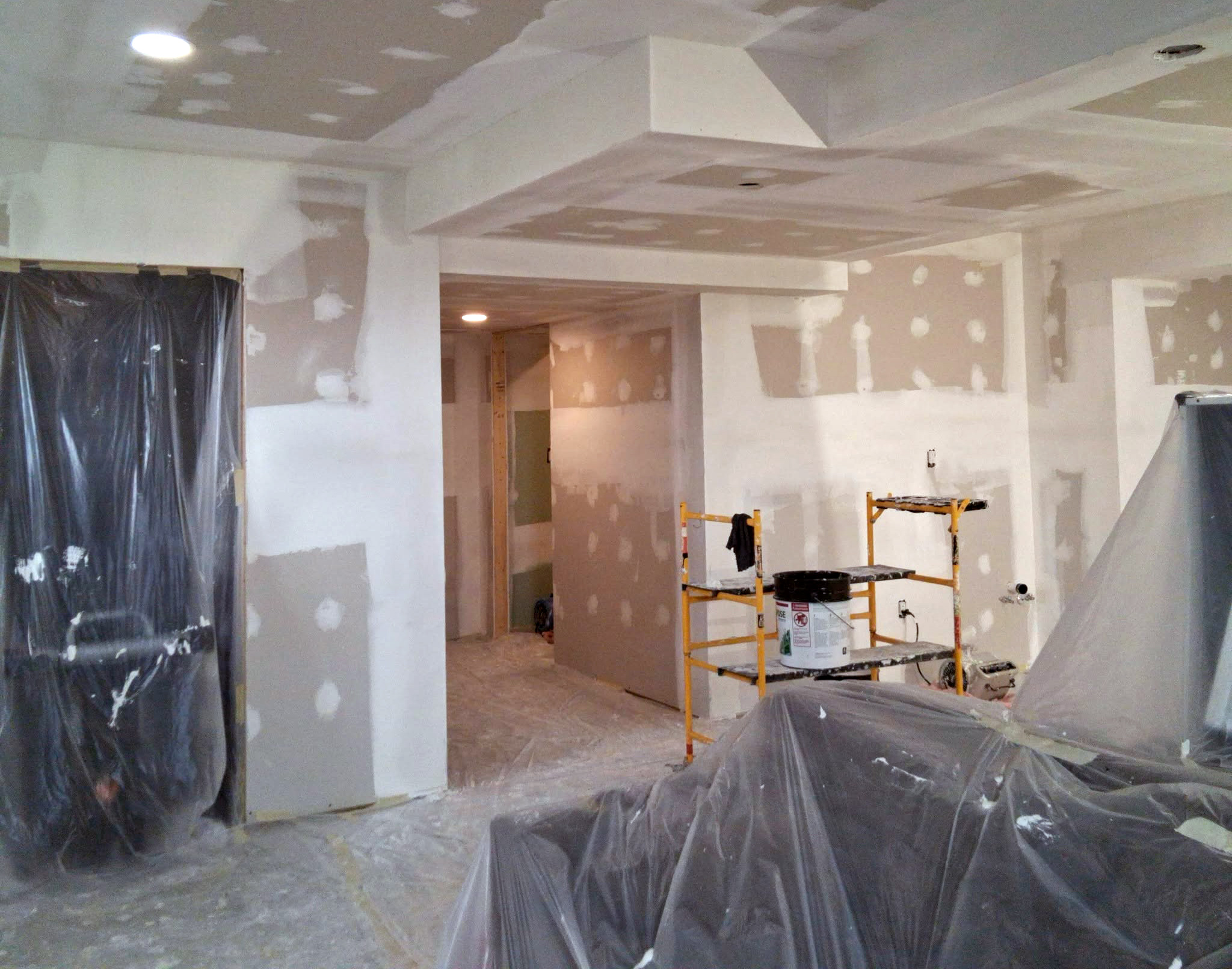 Drywall taped and mudded on the walls and a tray ceiling, with scaffolding still in the room